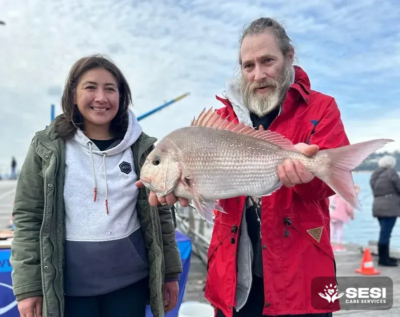 A support worker and participant on a pier, proudly showing off a large snapper caught on a fishing day