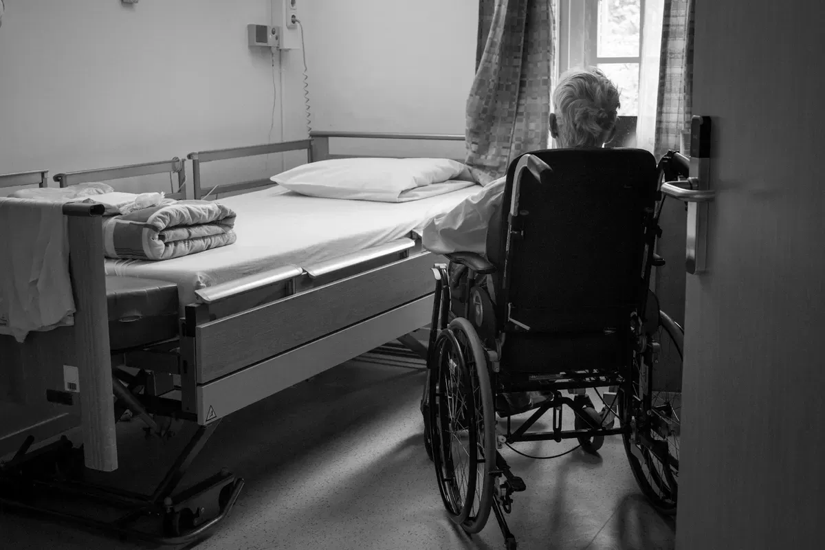An empty bed and wheelchair in a residential care room.