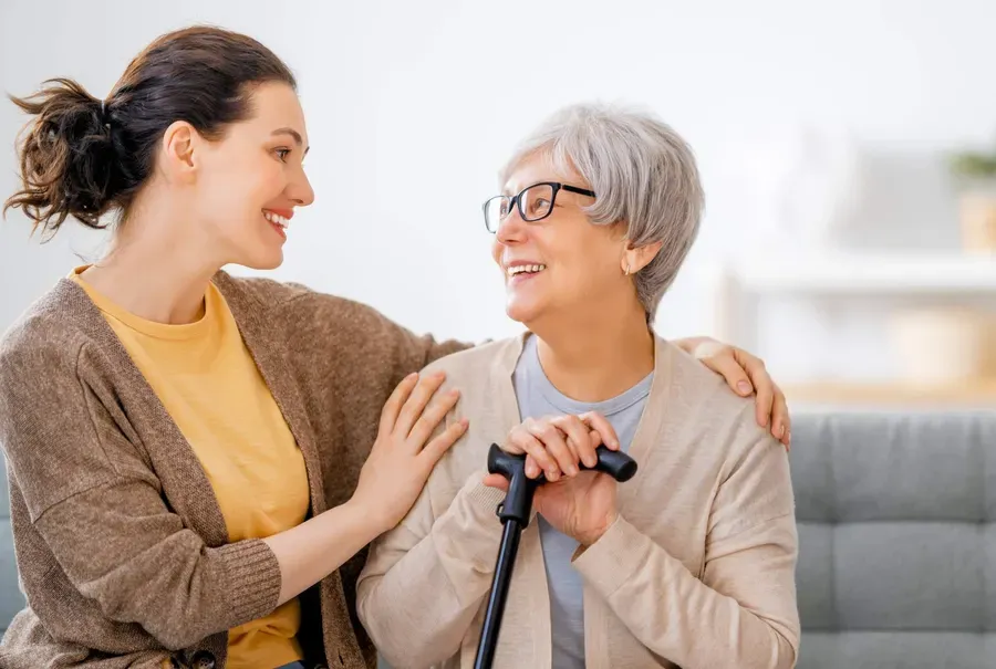 A support worker sitting close to an older woman with a walking cane, smiling together