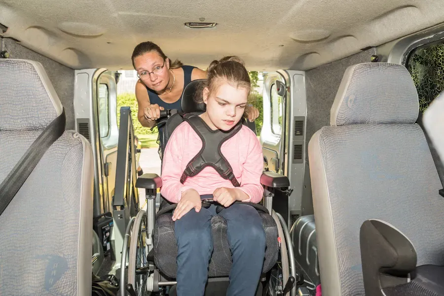 A support worker helping a young person in a wheelchair board an accessible van