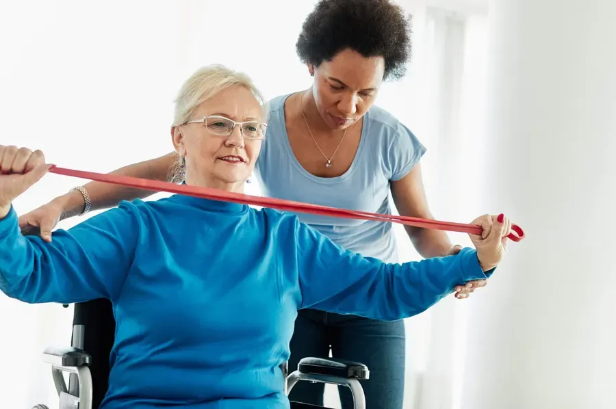 An occupational therapist guiding an older woman through a resistance-band exercise