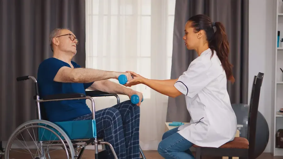 A physiotherapist supporting a man in a wheelchair through a dumbbell exercise